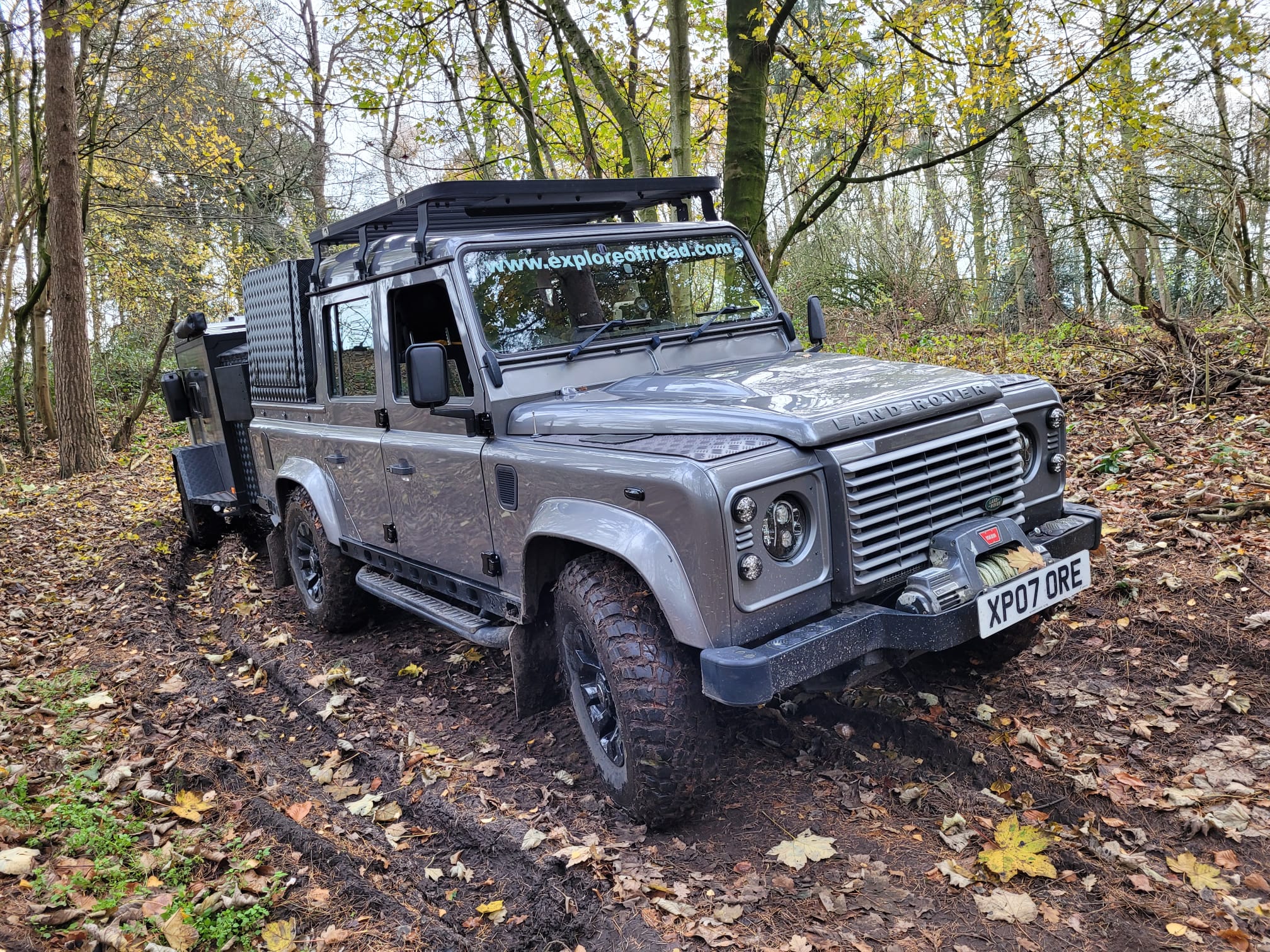 Explore Off-Road grey Land Rover Defender XP07 ORE with roof rack and front winch on a muddy autumn woodland track. Explore Off-Road grey Land Rover Defender XP07 ORE with roof rack and front winch on a muddy autumn woodland track.