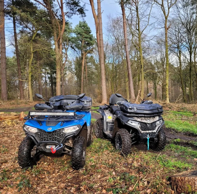 Two quad bikes, one blue and one dark grey, parked among trees on a woodland trail.